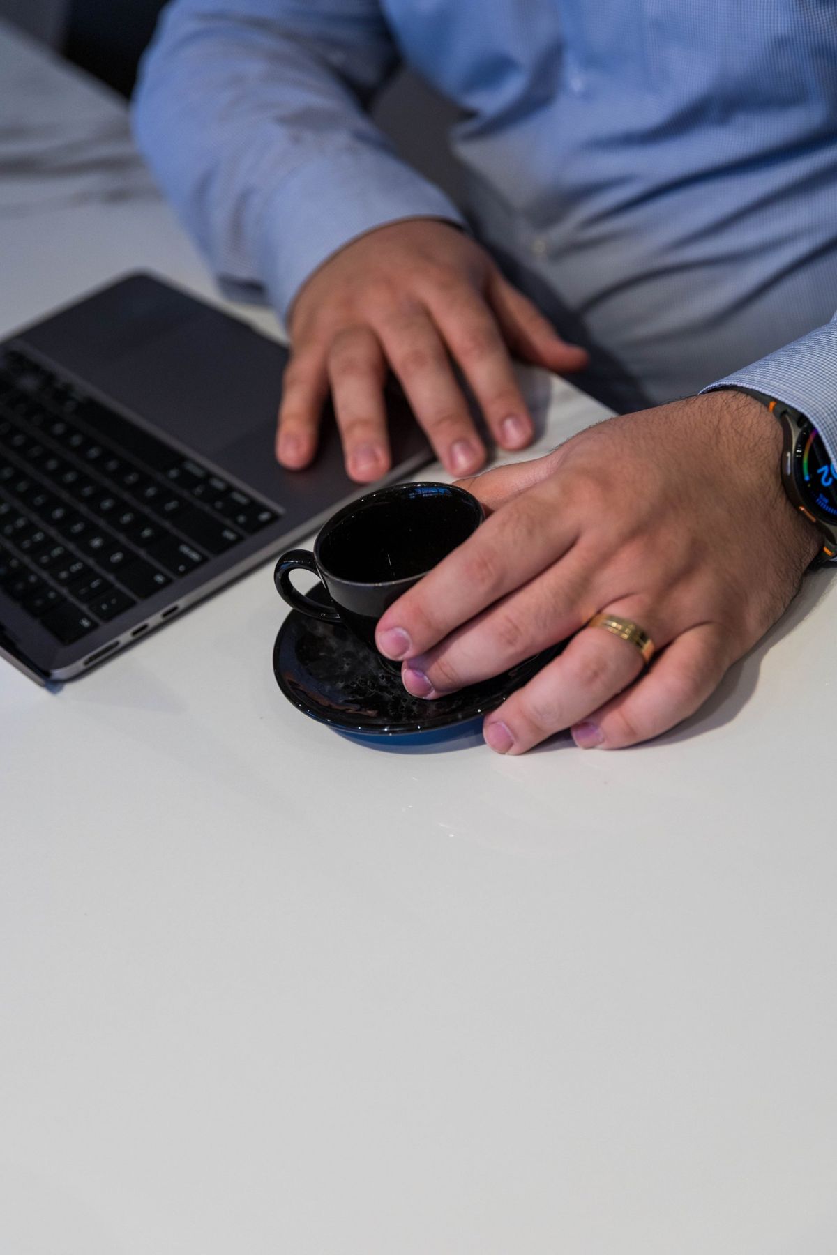Mãos sobre a mesa ao lado de um notebook e uma xícara de café